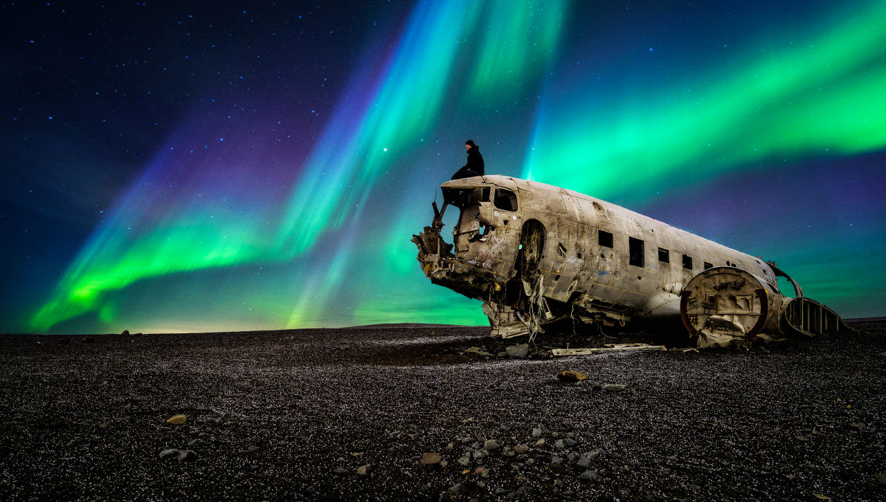 Guy sitting on destroyed airplane under the northern lights in Iceland